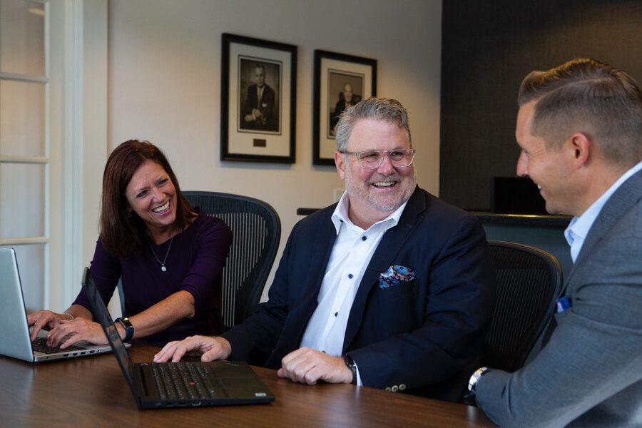 Two men and a woman seated at a table, with two laptops in front of them